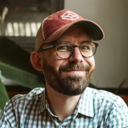 Me, Josh Collinsworth, an average white guy in a patterned button-up, with a beard, glasses, and a CodePen trucker hat.